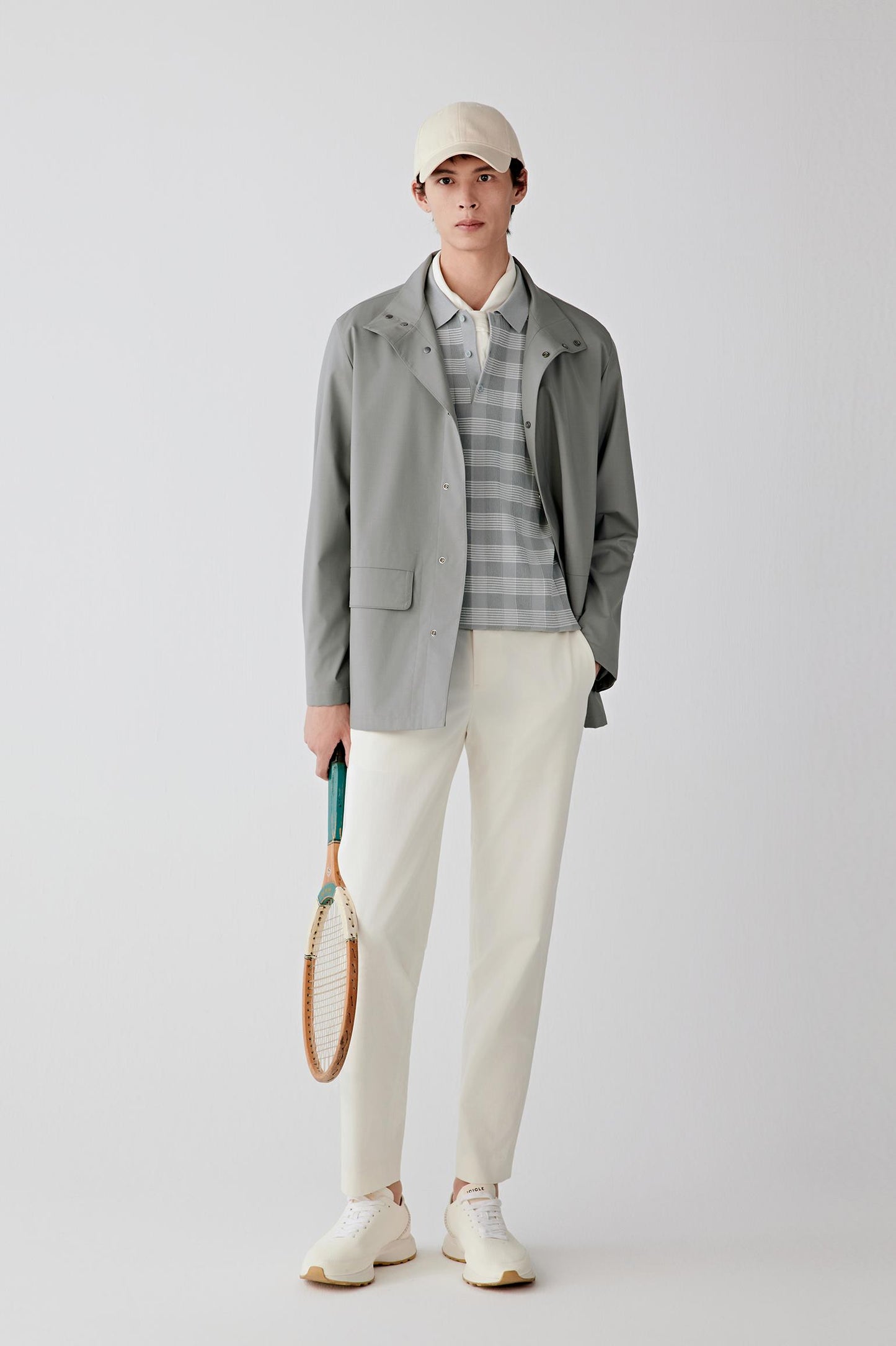 Full-length front view of a male model wearing a light grey worsted wool and silk jacket with stand collar and zip fastening, paired with off-white trousers.