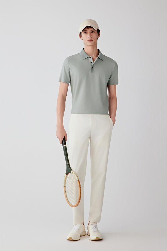 Man wearing a light grey cotton and silk jersey polo shirt with a relaxed fit, paired with off-white trousers and a cap; full-length front view showing the soft drape and clean silhouette.