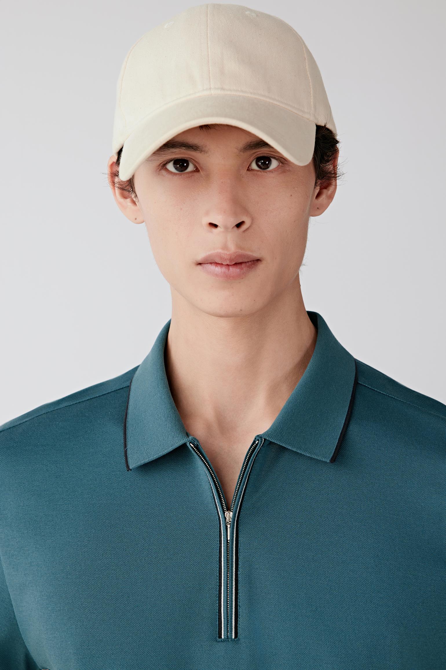 Close-up of the upper body showing the short collar, zip placket closure and clean neckline construction, with the fine piqué texture visible.