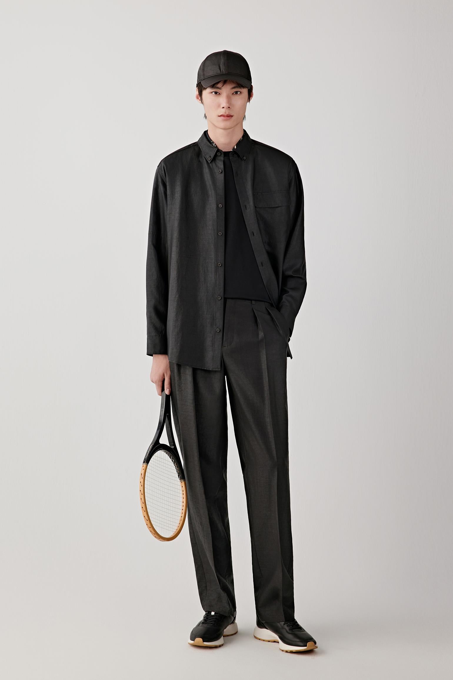 Man wearing a deep black Gambiered Canton gauze silk shirt with a relaxed straight cut and classic collar, styled with matching trousers; full-length front view showing the soft drape, slightly textured surface and fluid silhouette.