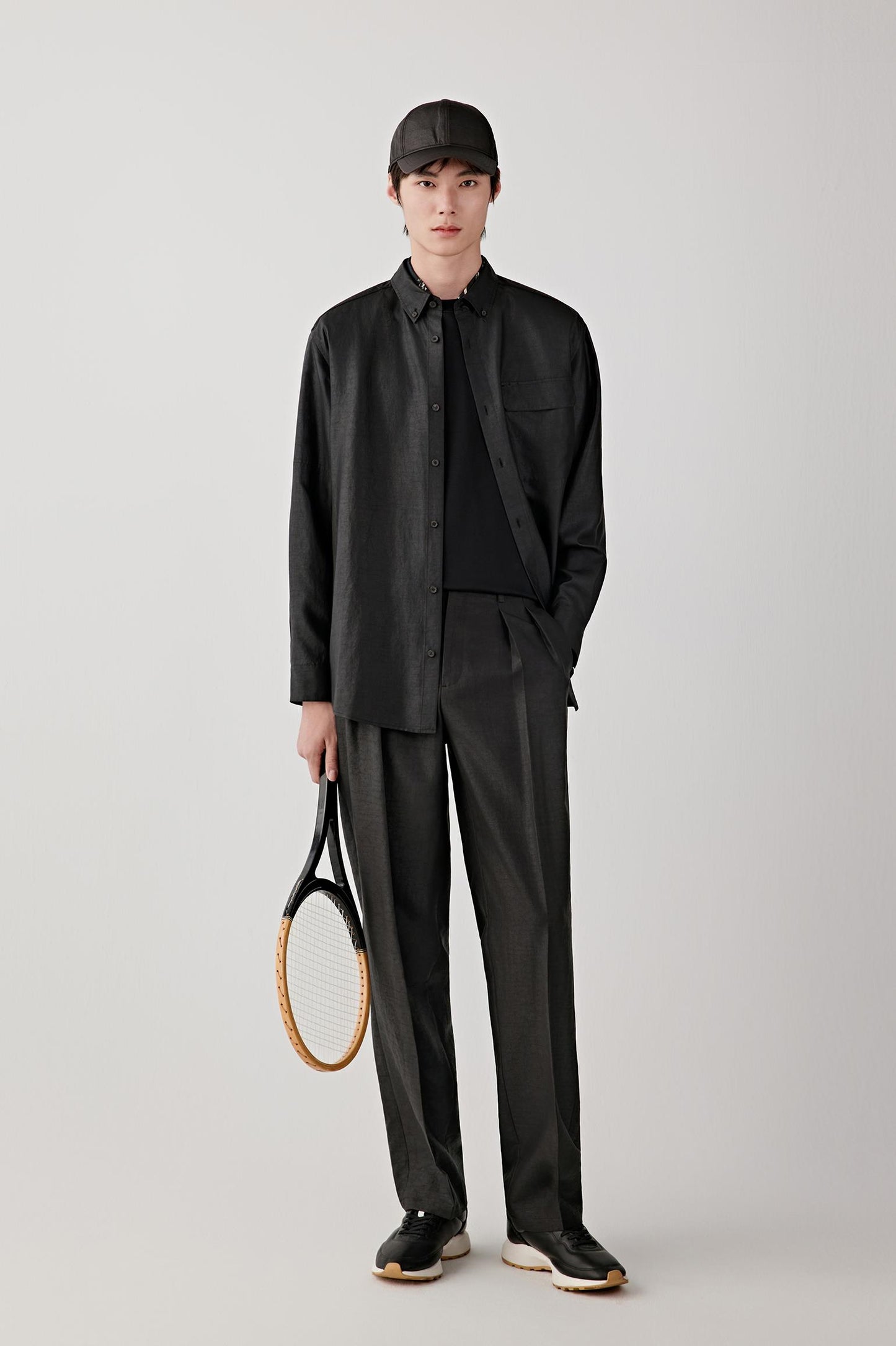 Man wearing deep black Gambiered Canton gauze silk trousers with a straight, relaxed fit, paired with a matching jacket and light inner layer; full-length front view showing the fluid drape and slightly matte, textured surface.