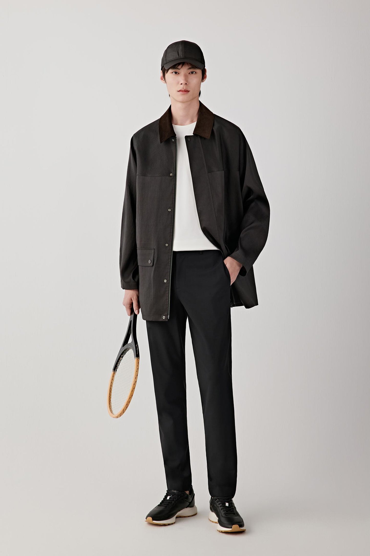 Man wearing a deep black Gambiered Canton gauze silk jacket with a straight, relaxed cut and classic collar, styled with black trousers and a light inner layer; full-length front view showing the fluid drape, slightly matte sheen and lightweight structure.