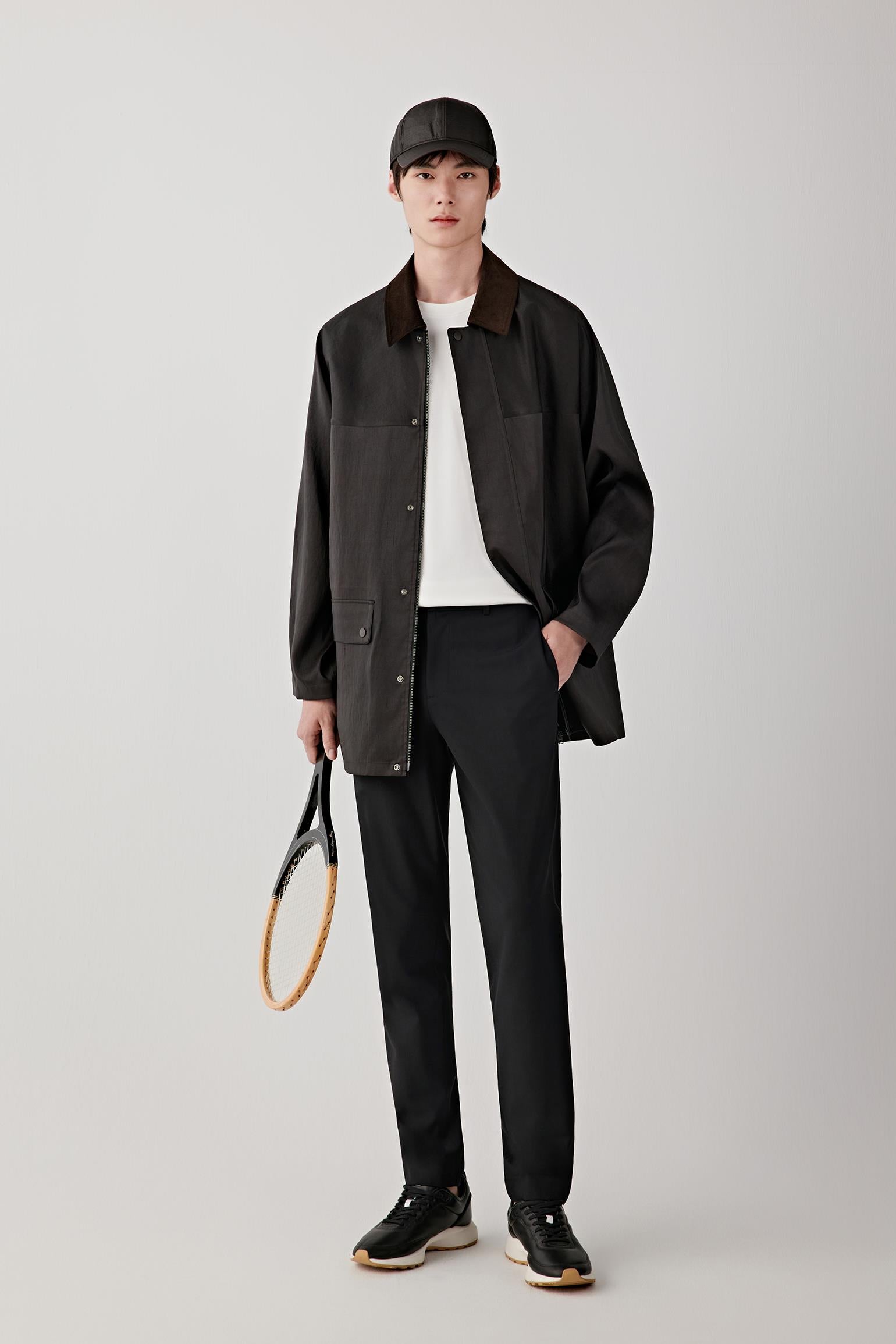 Man wearing a deep black Gambiered Canton gauze silk jacket with a straight, relaxed cut and classic collar, styled with black trousers and a light inner layer; full-length front view showing the fluid drape, slightly matte sheen and lightweight structure.