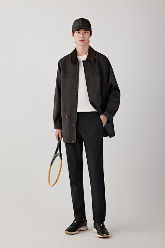Man wearing a deep black Gambiered Canton gauze silk jacket with a straight, relaxed cut and classic collar, styled with black trousers and a light inner layer; full-length front view showing the fluid drape, slightly matte sheen and lightweight structure.