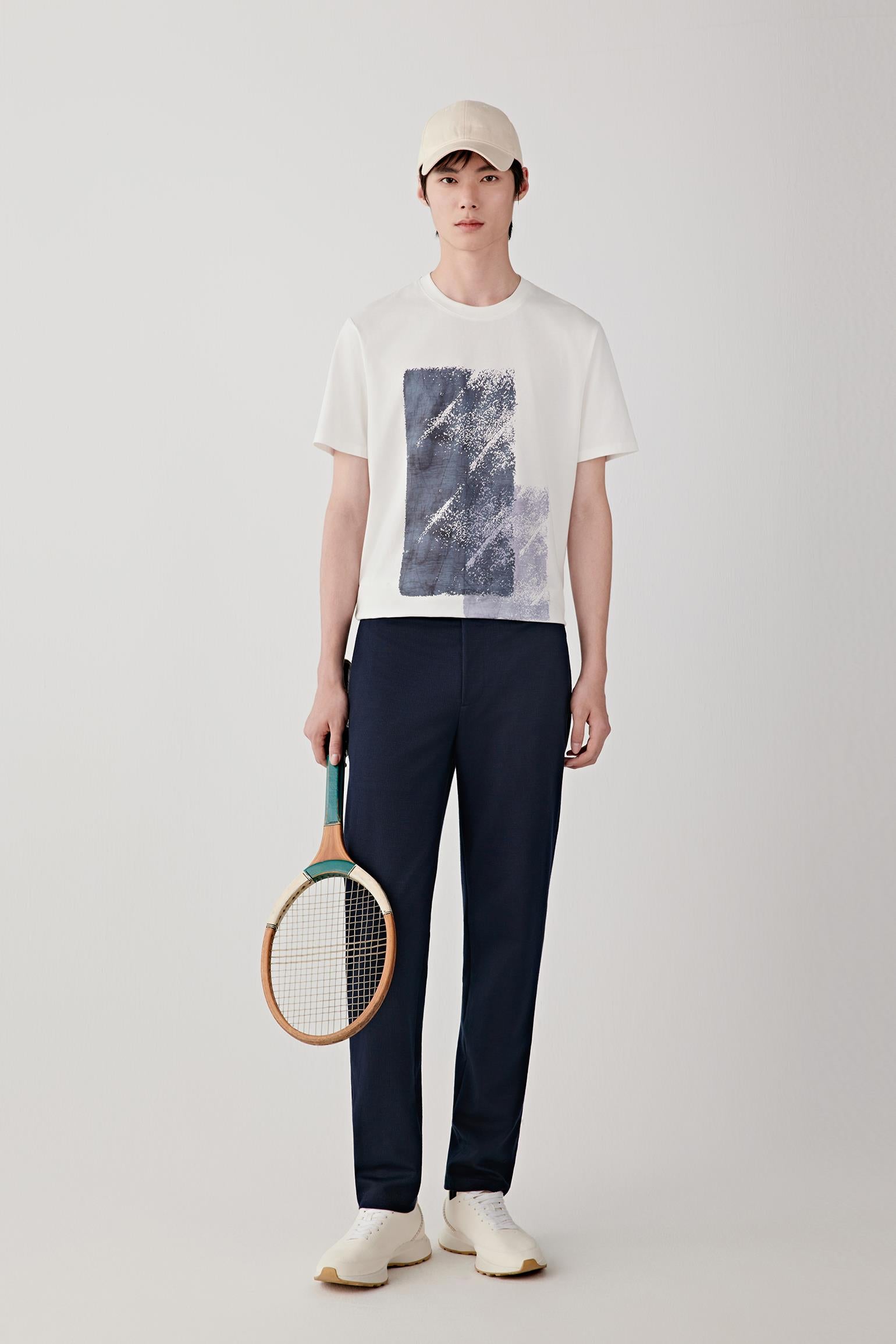 Man wearing navy ramie cotton and jacquard jersey trousers with a mid-rise waist and straight-leg cut, styled with a white T-shirt and cap; full-length front view showing the clean silhouette, lightweight structure and straight fall from hip to ankle.