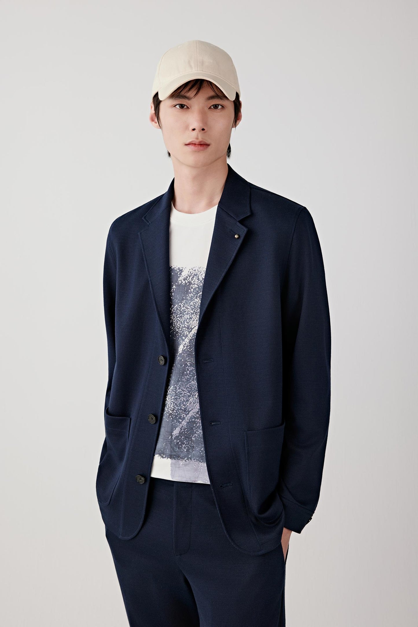 Front three-quarter view highlighting the button fastening, patch pockets and relaxed tailoring through the torso, with a soft, flexible drape.