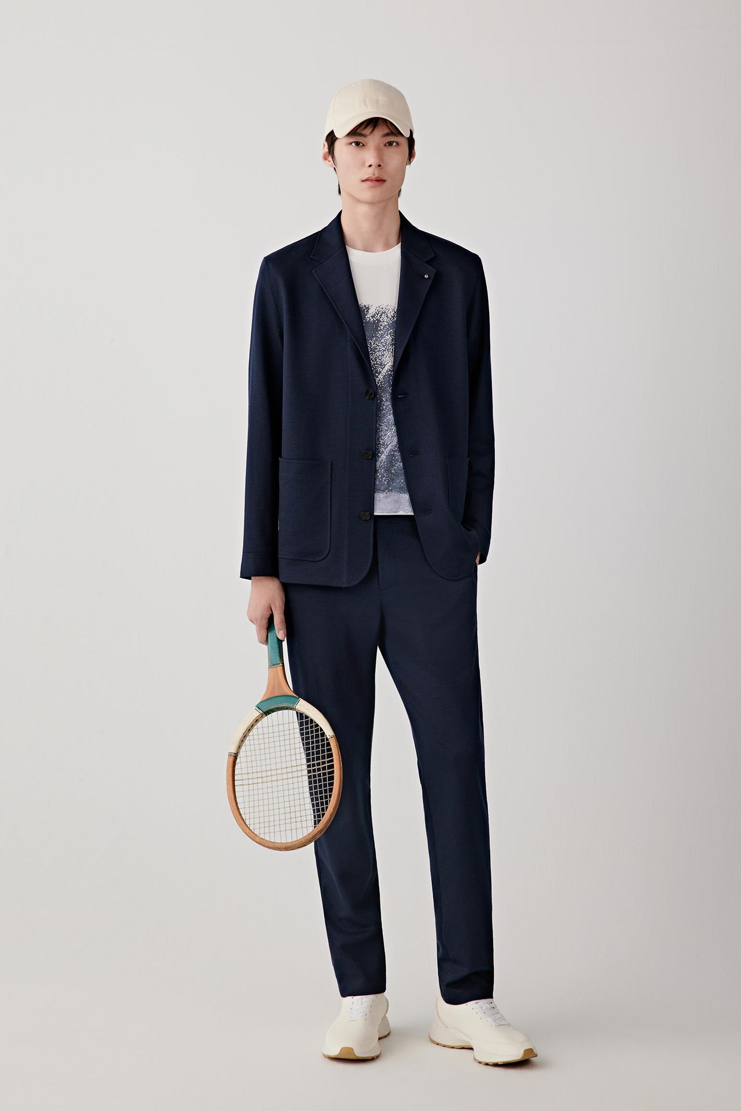 Man wearing a navy ramie cotton and jacquard jersey jacket with a tailored straight cut and notched lapel, styled with matching trousers, white T-shirt and cap; full-length front view showing the clean silhouette, lightweight structure and matte textured finish.