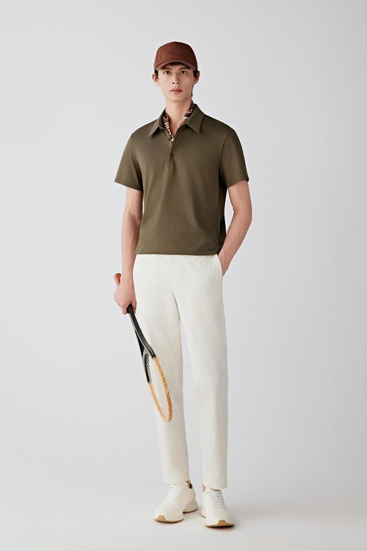 Full-length front view of a man standing facing forward wearing an olive green cotton jersey polo shirt paired with light-colored trousers, highlighting the straight silhouette, clean proportions and the smooth, lightweight jersey fabric with a soft, fluid drape