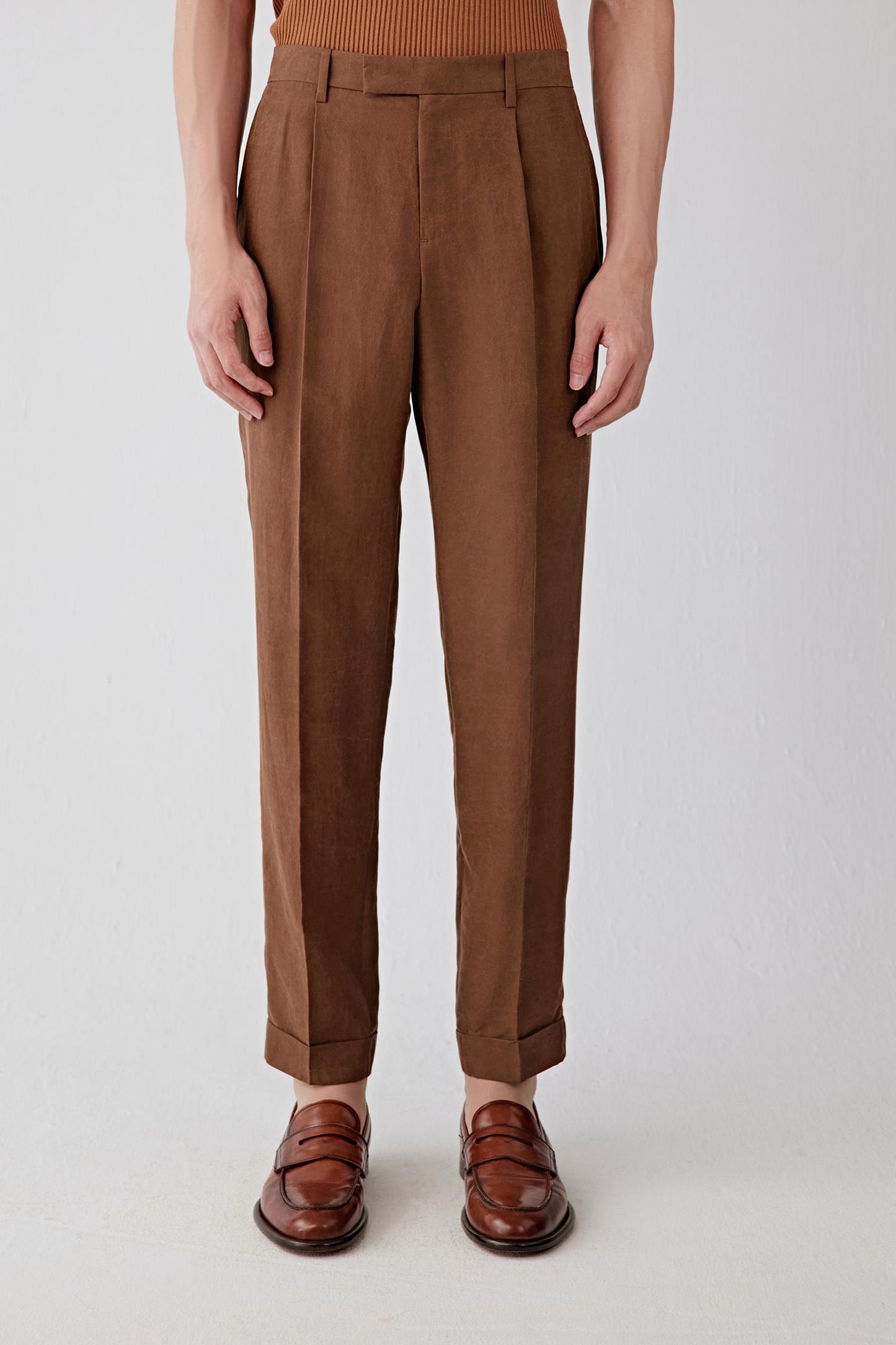 Mid-length front view focusing on the waist and upper leg, emphasizing the structured waistband, front pleats and precise construction, with the fabric revealing a slightly firm hand and a softly textured surface characteristic of the Gambiered Canton gauze technique