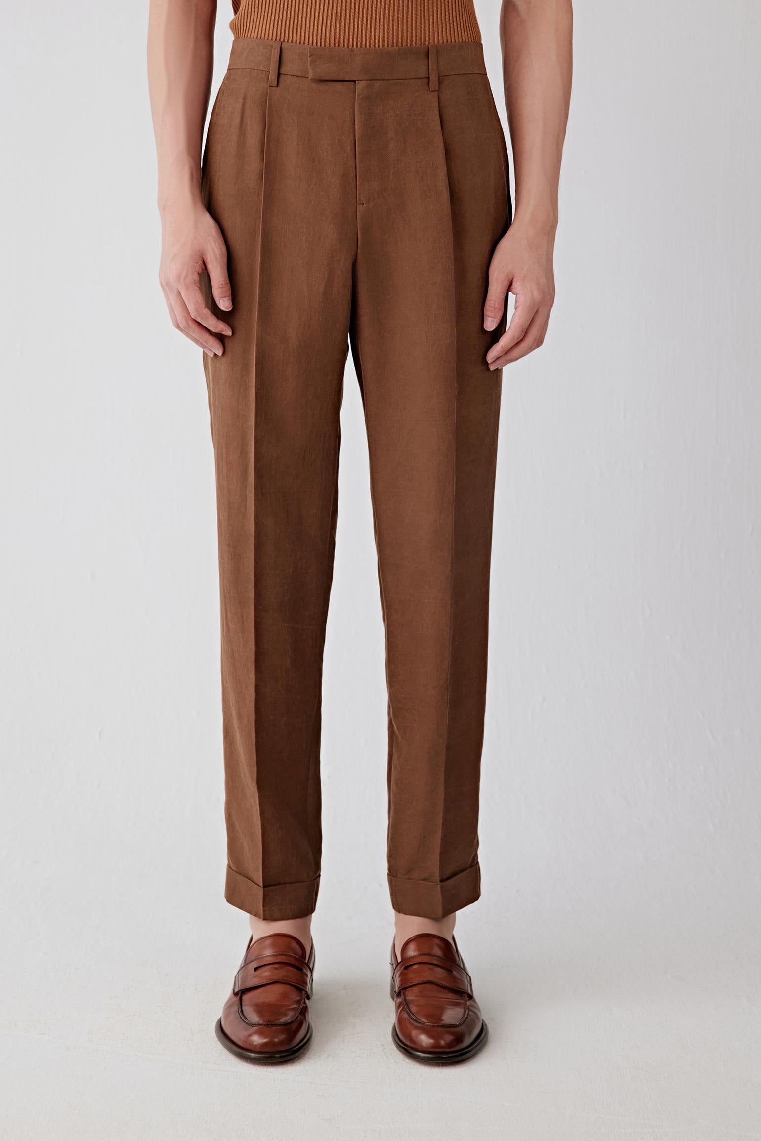 Mid-length front view focusing on the waist and upper leg, emphasizing the structured waistband, front pleats and precise construction, with the fabric revealing a slightly firm hand and a softly textured surface characteristic of the Gambiered Canton gauze technique