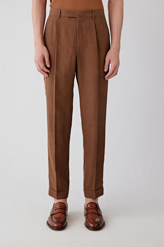 Mid-length front view focusing on the waist and upper leg, emphasizing the structured waistband, front pleats and precise construction, with the fabric revealing a slightly firm hand and a softly textured surface characteristic of the Gambiered Canton gauze technique