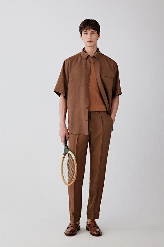 Full-length front view of a man standing facing forward wearing a brown Gambiered Canton gauze short-sleeve shirt paired with matching trousers, highlighting the straight, relaxed silhouette, clean proportions and the matte fabric surface with subtle tonal depth created by the traditional dyeing process