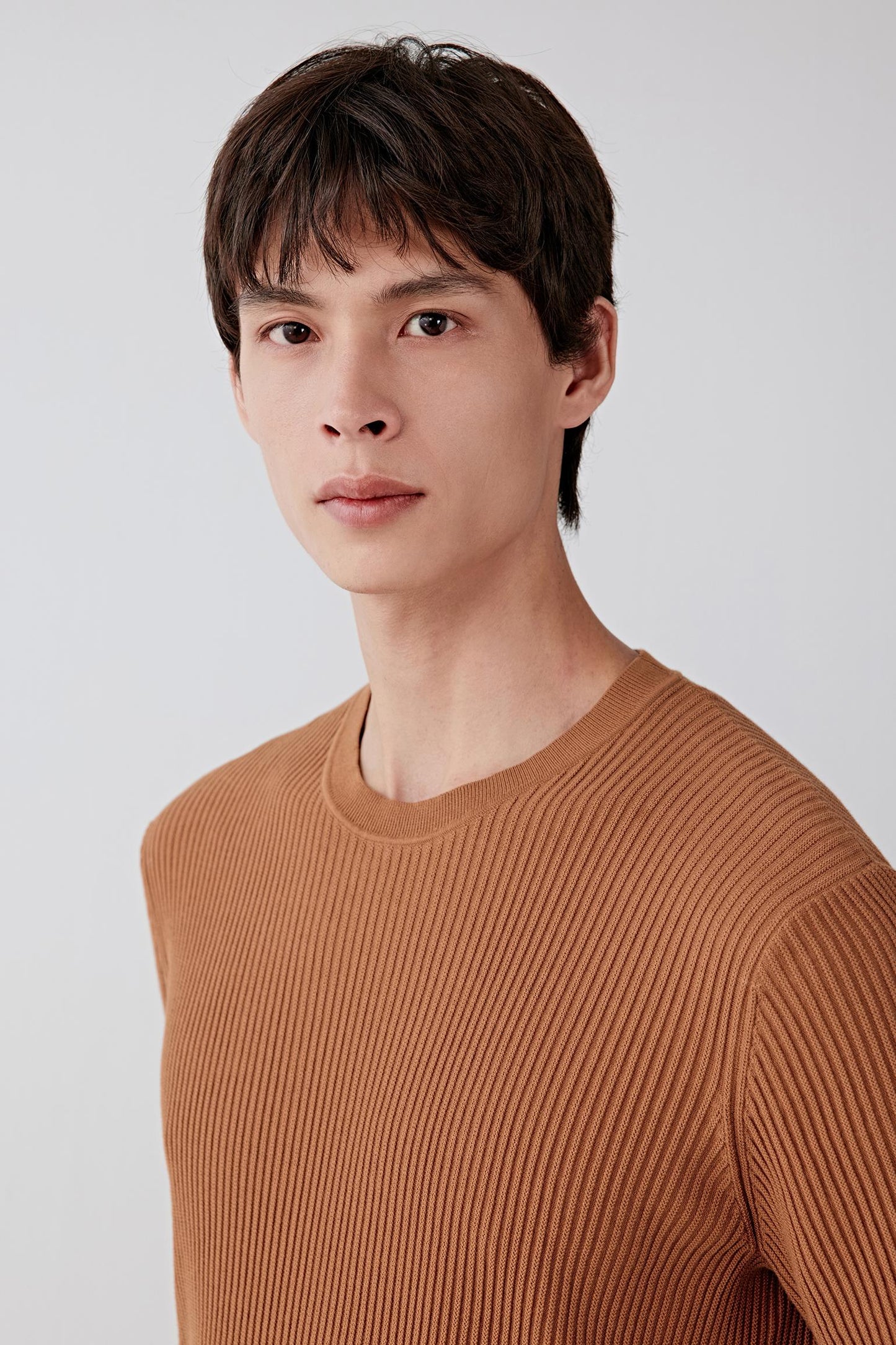 Close-up portrait focusing on the neckline and upper chest, showing the round neckline, clean finishing and the fine, regular ribbed knit structure, with the brown shade enhancing depth in the texture