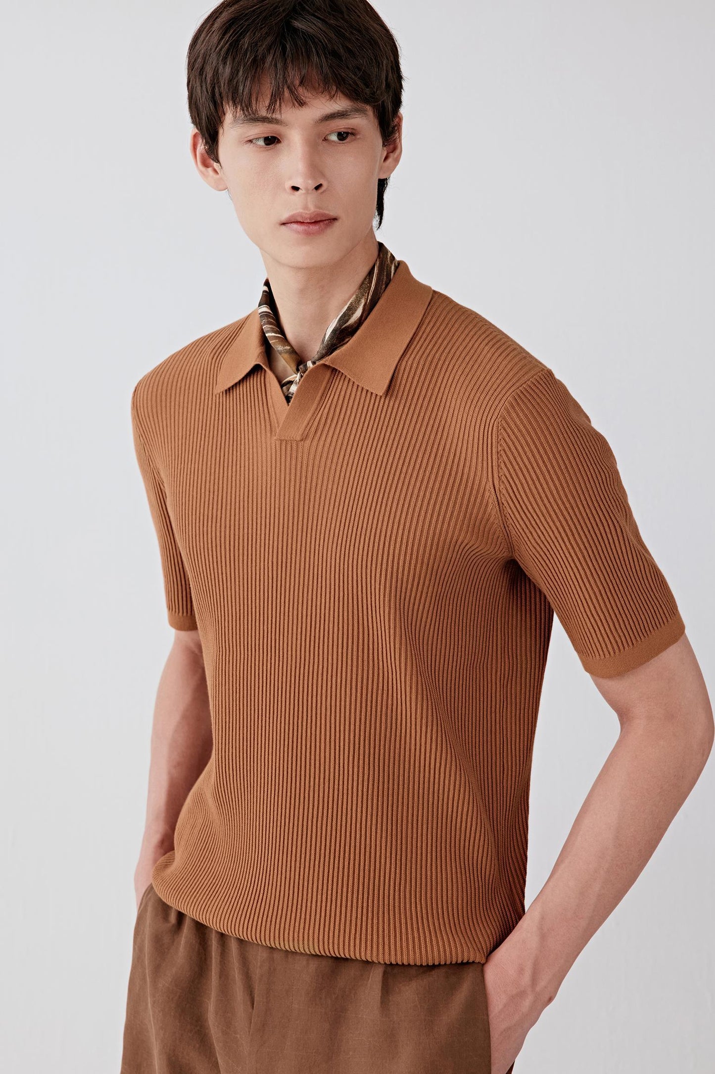 Close-up portrait focusing on the neckline and upper chest, detailing the short collar construction, V opening and the regularity of the ribbed knit, with the brown shade revealing subtle tonal variations in the texture