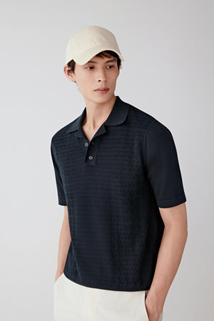Front view of a man wearing a deep black pullover in fine-spun cotton, highlighting the lightweight knit structure, smooth matte surface and soft hand of the fabric. The dark shade emphasizes the regularity of the knit construction.