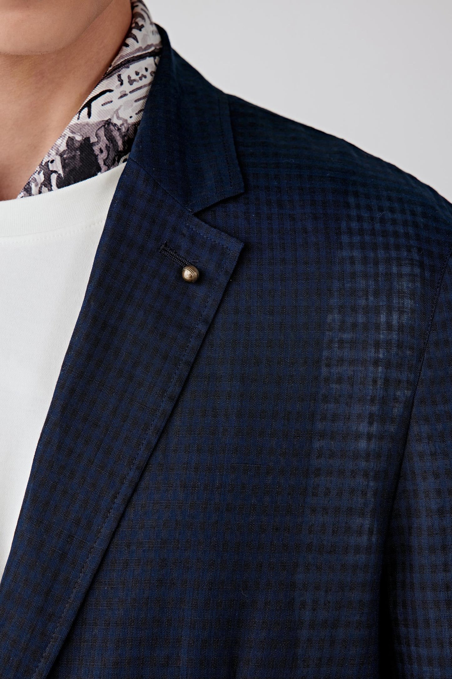 Close-up portrait focusing on the notch lapel and front construction, detailing the woven texture, fine check surface and clean finishing of the linen and cotton blend.