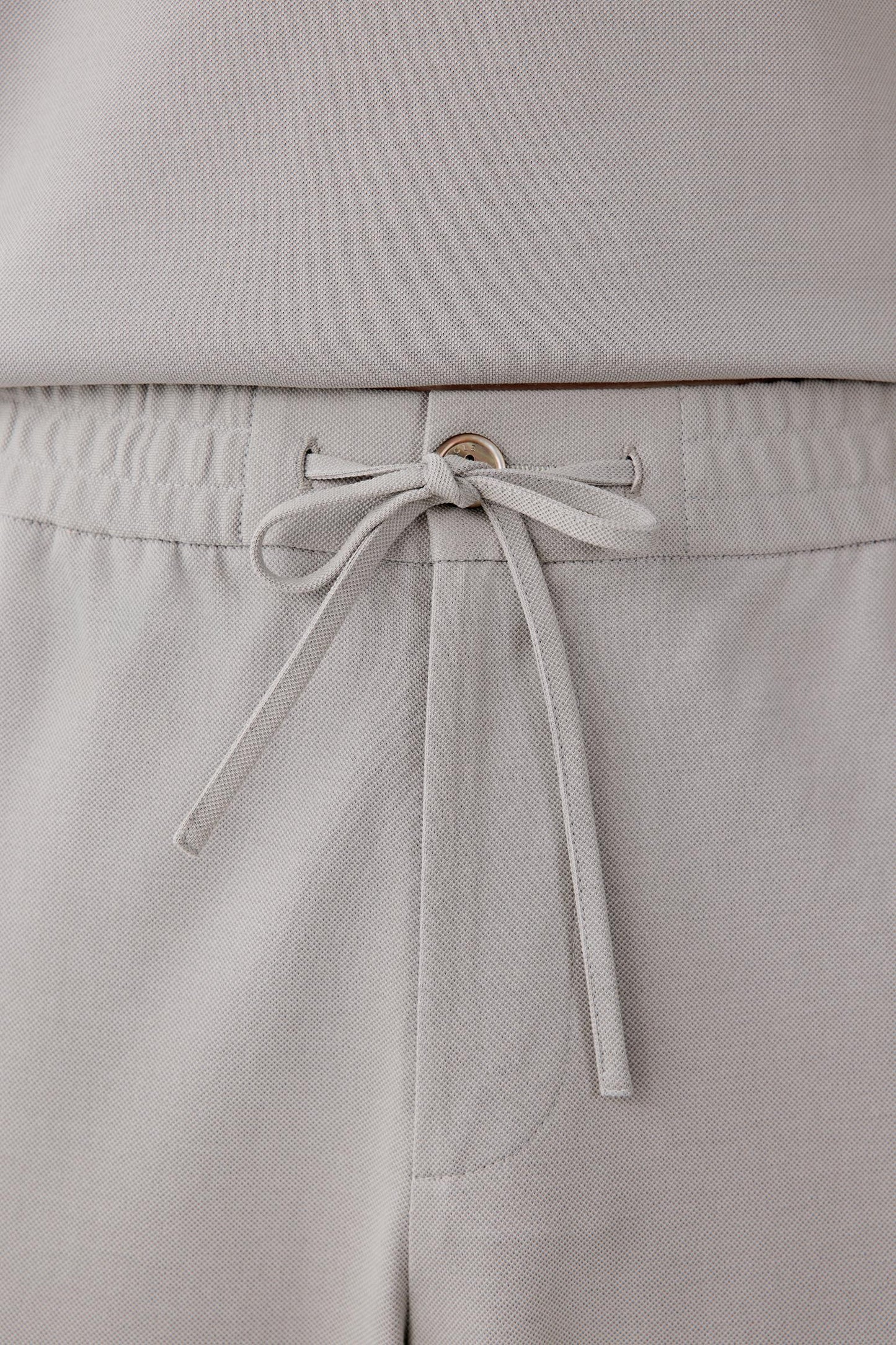 Close-up of the waistband detailing the elasticated construction, drawstring fastening and gathered texture of the cotton piqué jersey.