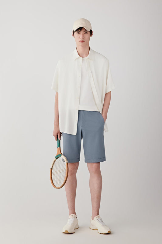 Front view of a man wearing stone blue shorts in cotton piqué jersey, highlighting the softly textured surface, lightweight structure and relaxed drape of the fabric. The piqué construction reveals subtle texture and a soft matte appearance.