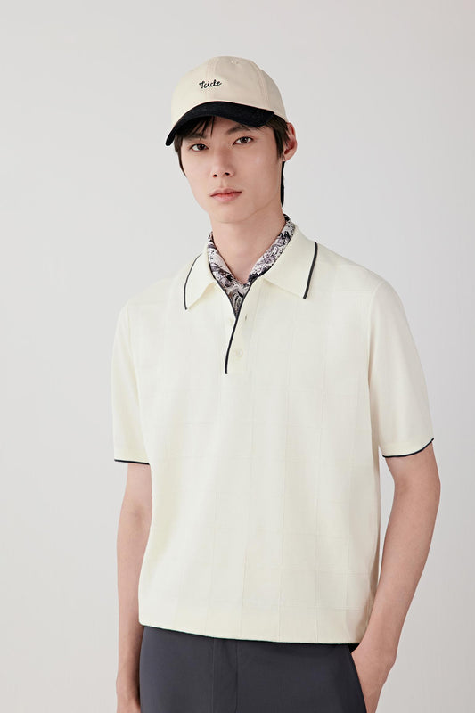 Three-quarter view showing the polo shirt styled with tailored dark trousers. The image emphasizes the fluid drape of the cotton knit, the short sleeves and the balanced proportions of the garment.