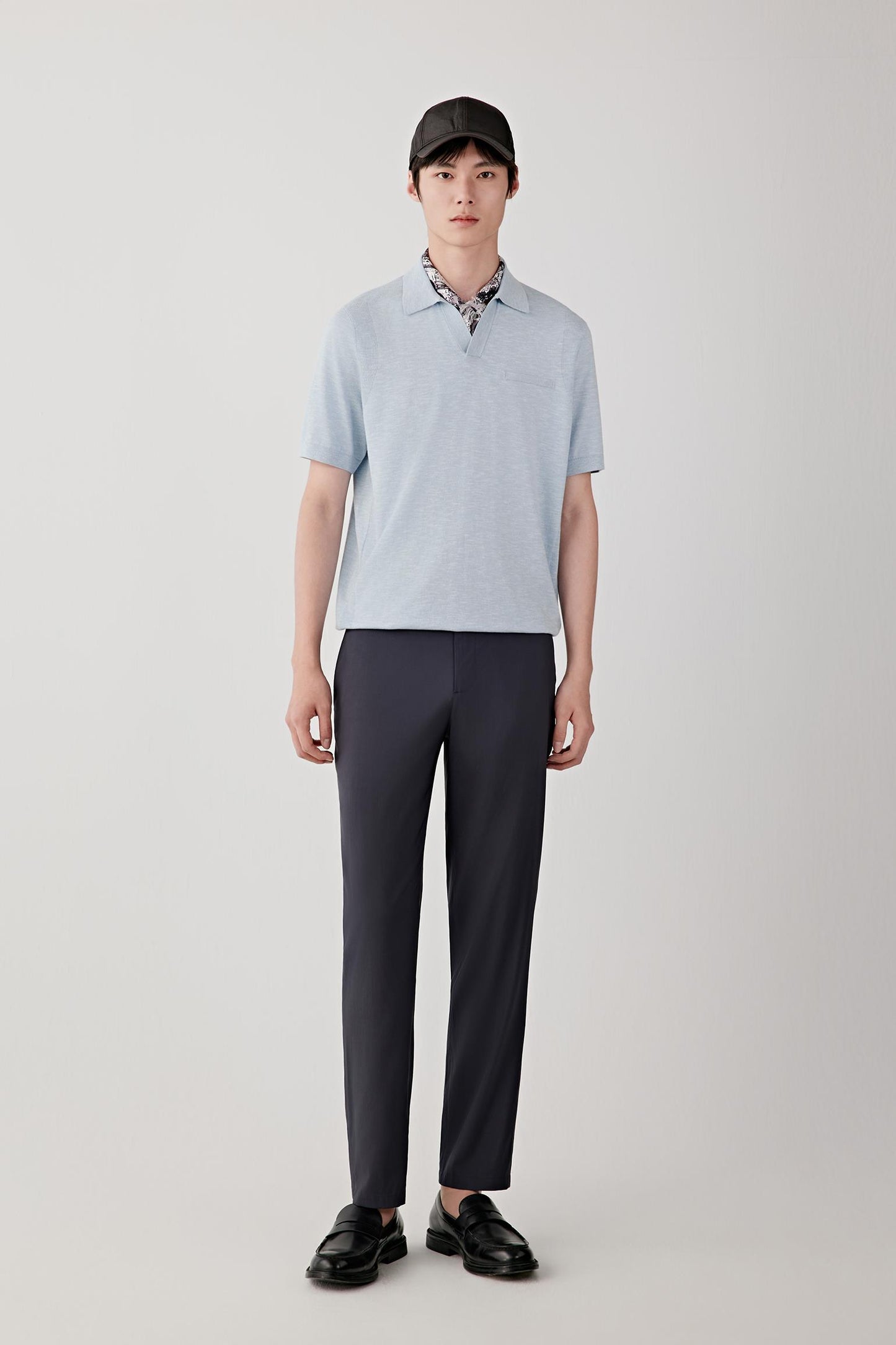 Full-length view showing the polo shirt paired with tailored trousers. The image emphasizes the clean proportions, fluid drape and lightweight structure of the knit while illustrating the garment's relaxed yet refined appearance.