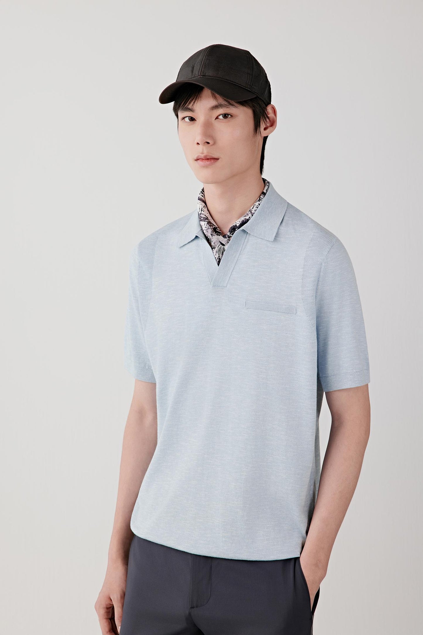 Front view of a man wearing a blue melange polo shirt in cotton and silk slub yarn, highlighting the relaxed silhouette, lightweight knit construction and softly textured surface. The slub yarn creates subtle irregularities and tonal variation throughout the fabric.