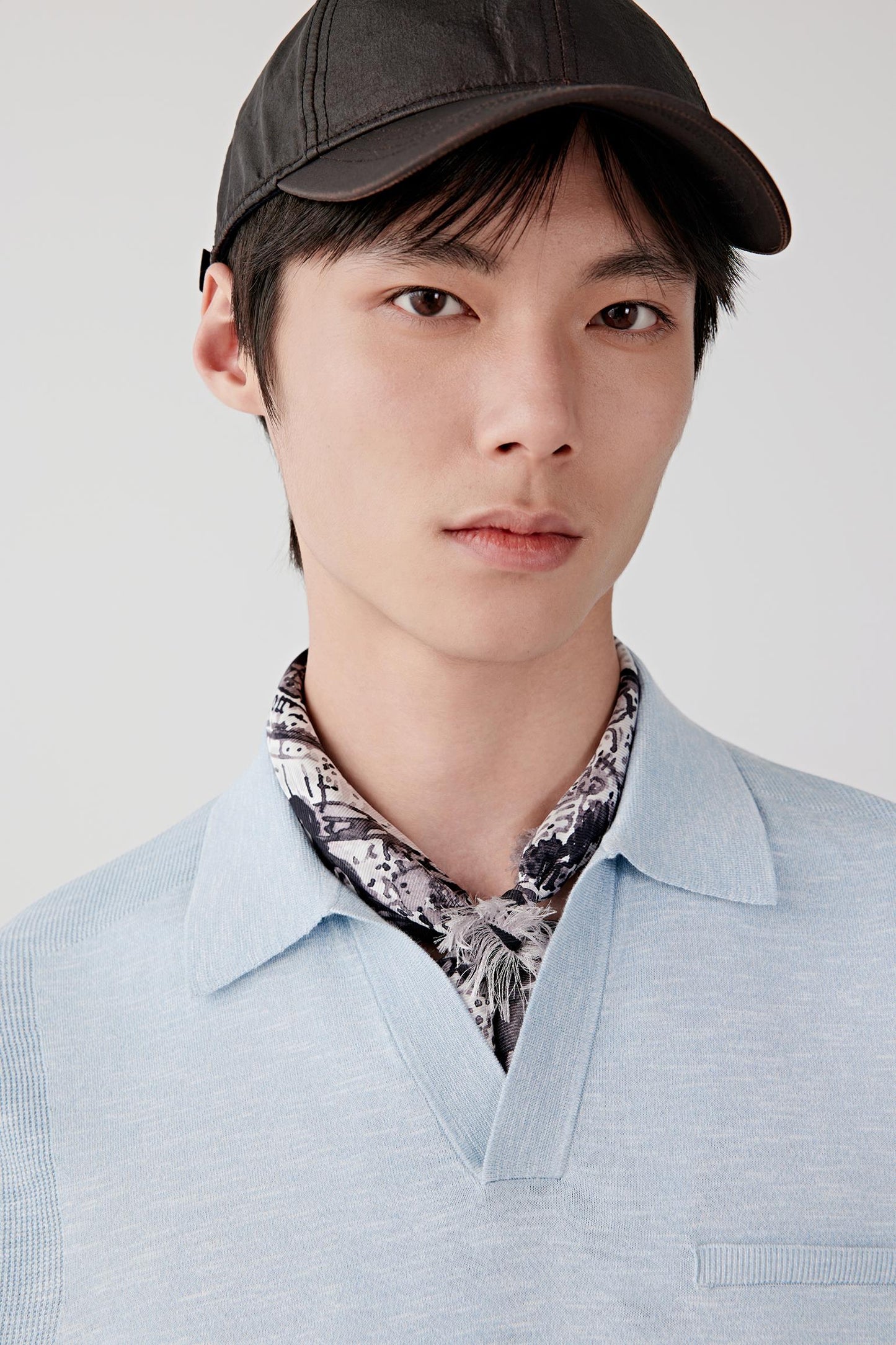 Close-up portrait focusing on the open polo collar, neckline and upper body construction. The image reveals the characteristic slub texture, soft surface and subtle tonal depth of the blue melange knit.