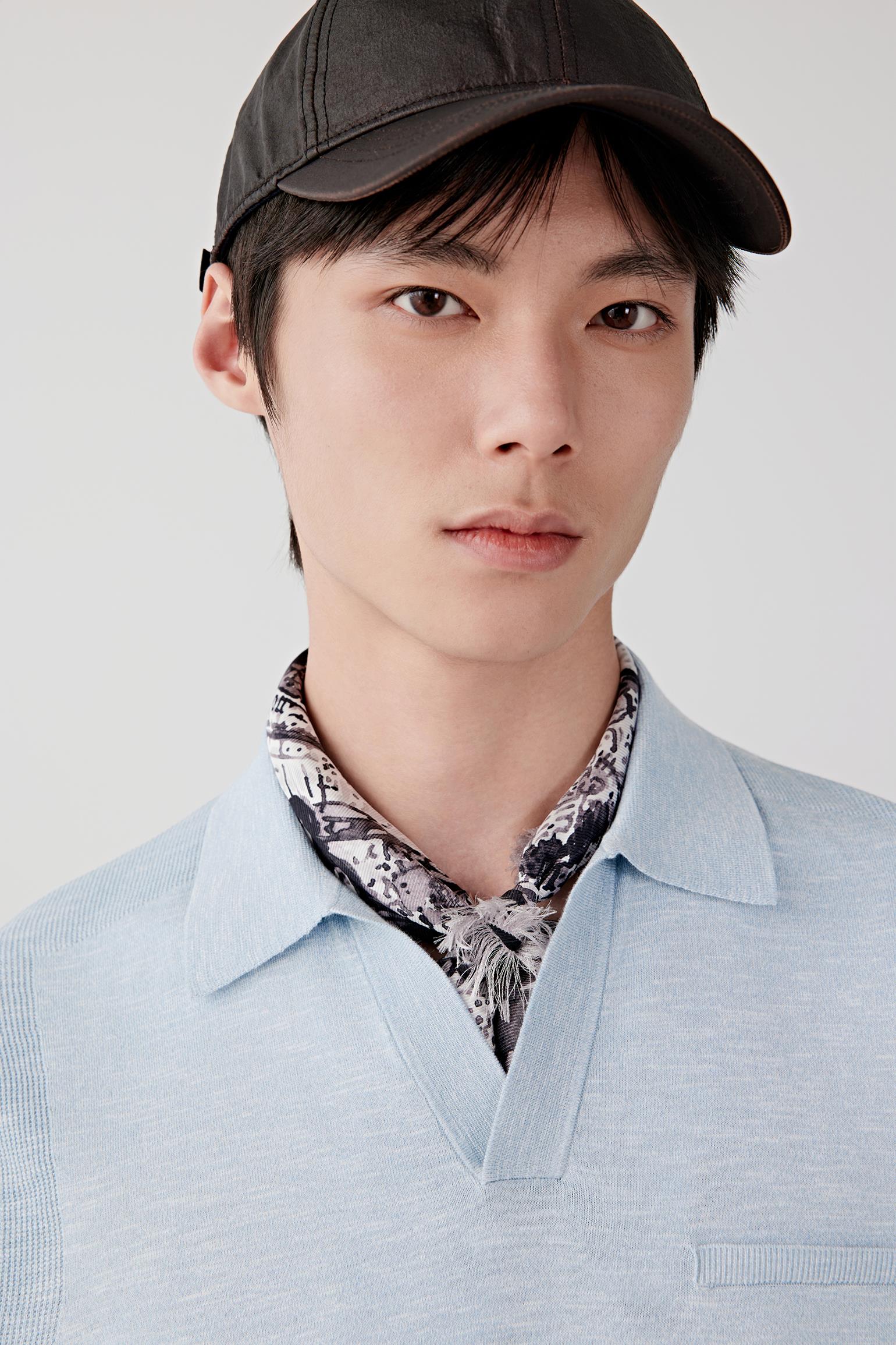 Close-up portrait focusing on the open polo collar, neckline and upper body construction. The image reveals the characteristic slub texture, soft surface and subtle tonal depth of the blue melange knit.