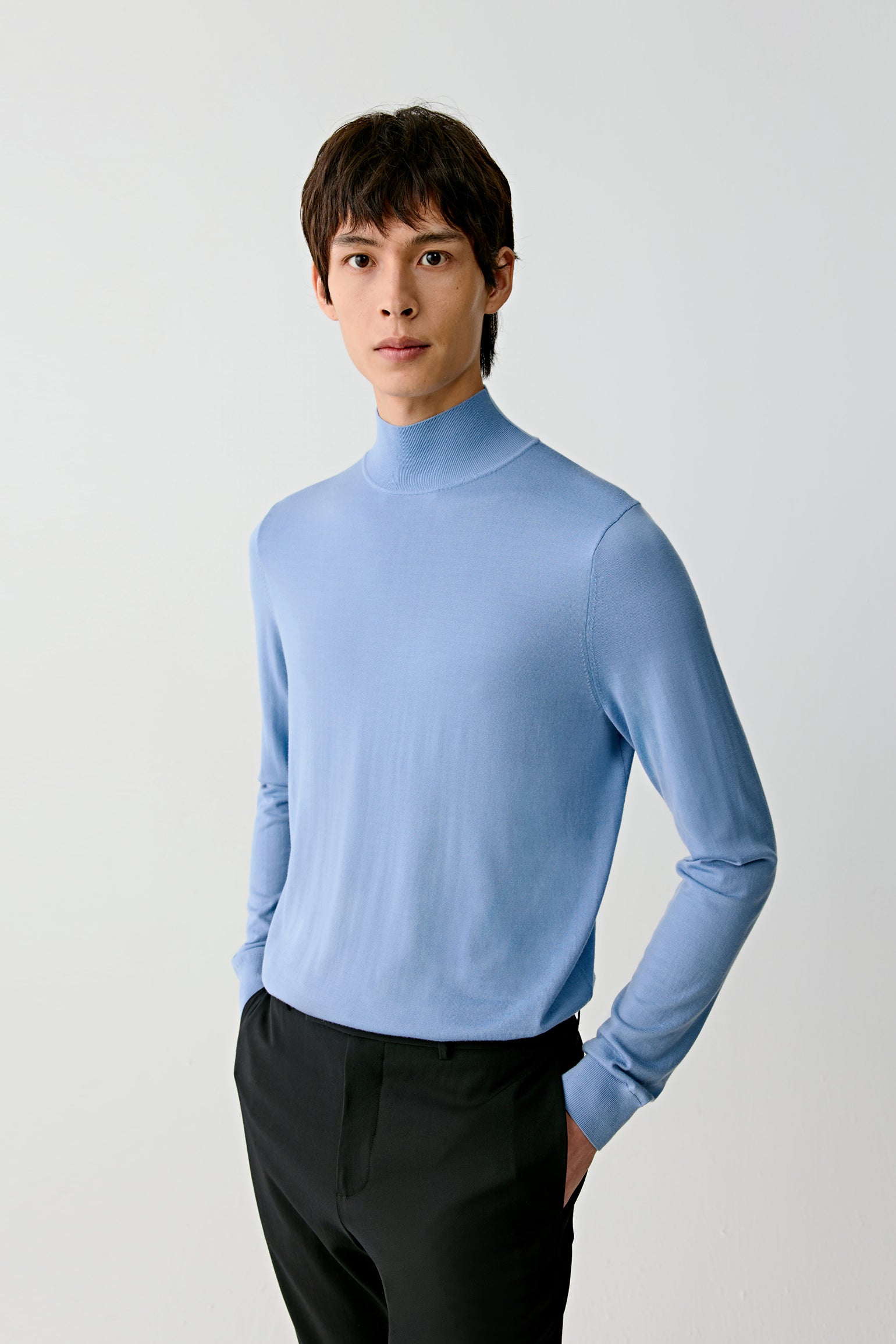 Man wearing a light blue turtleneck sweater against a white background