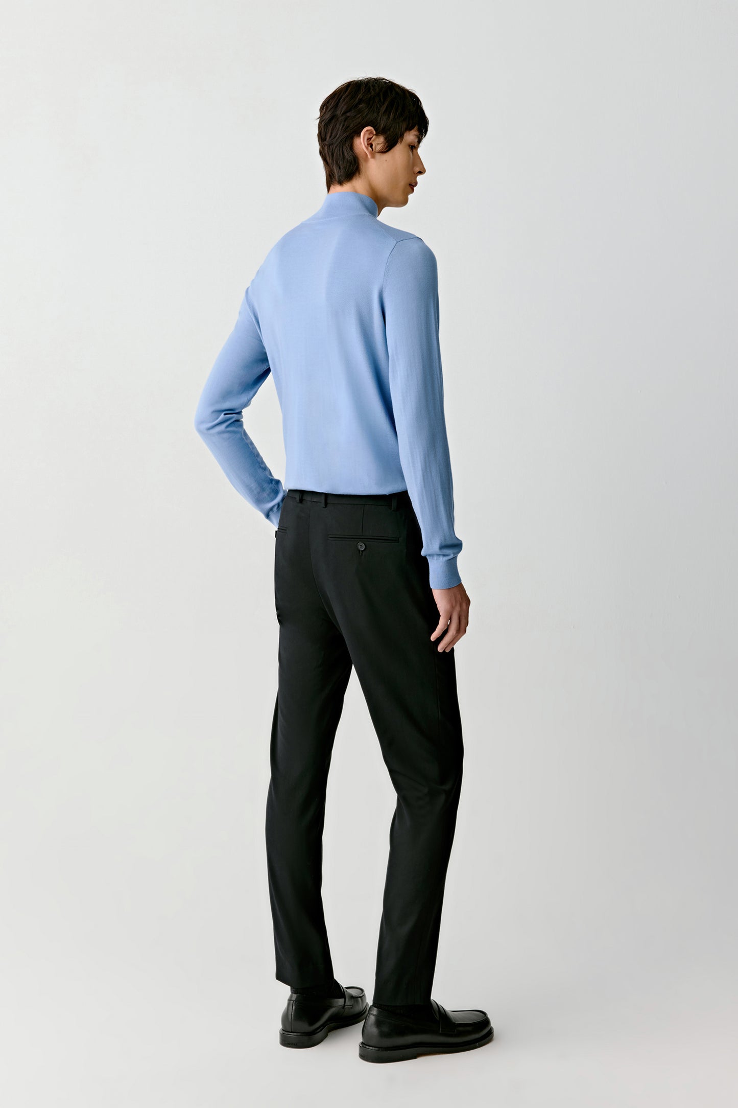 Person wearing a light blue sweater and black pants on a white background