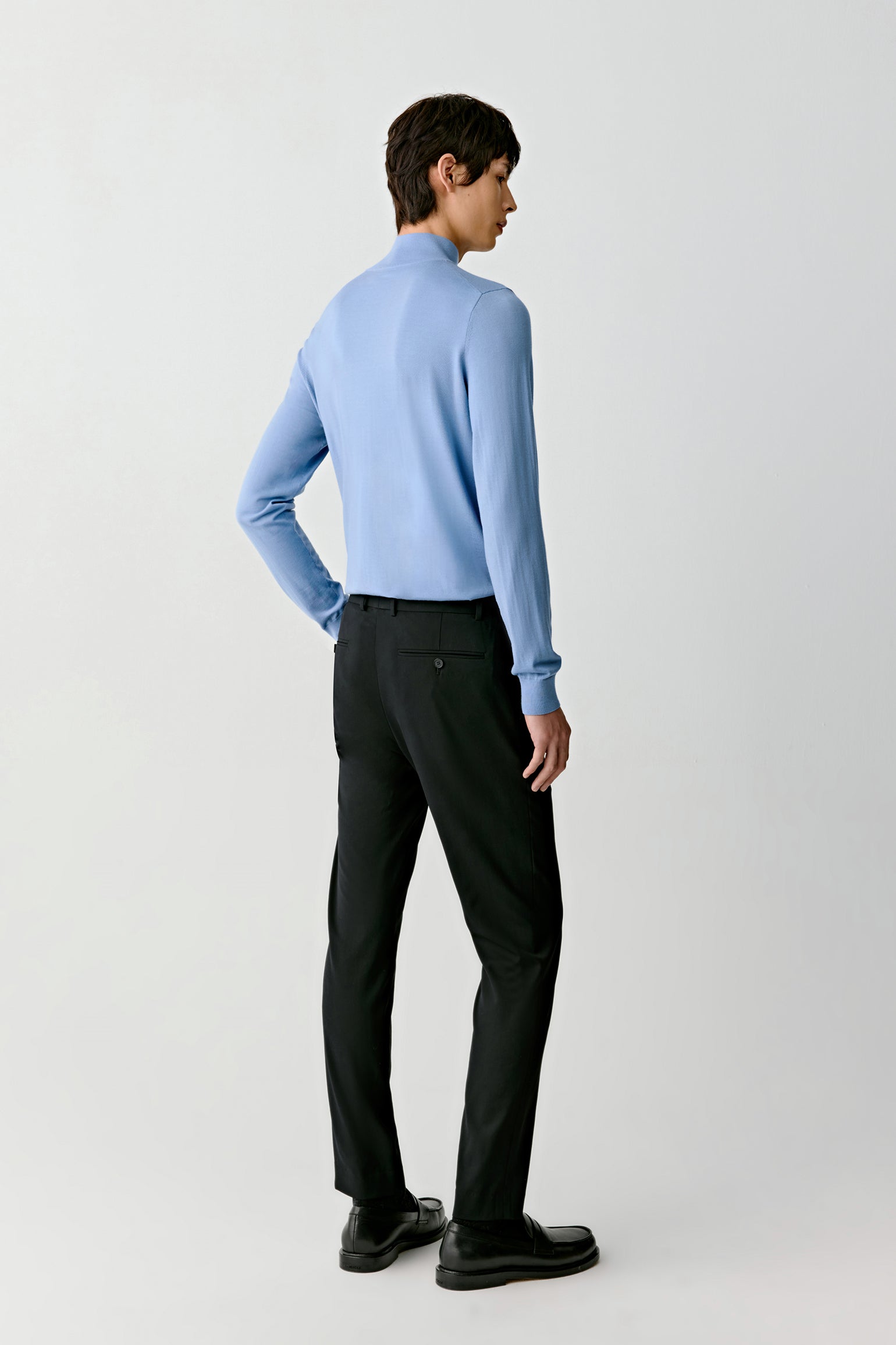 Person wearing a light blue sweater and black pants on a white background