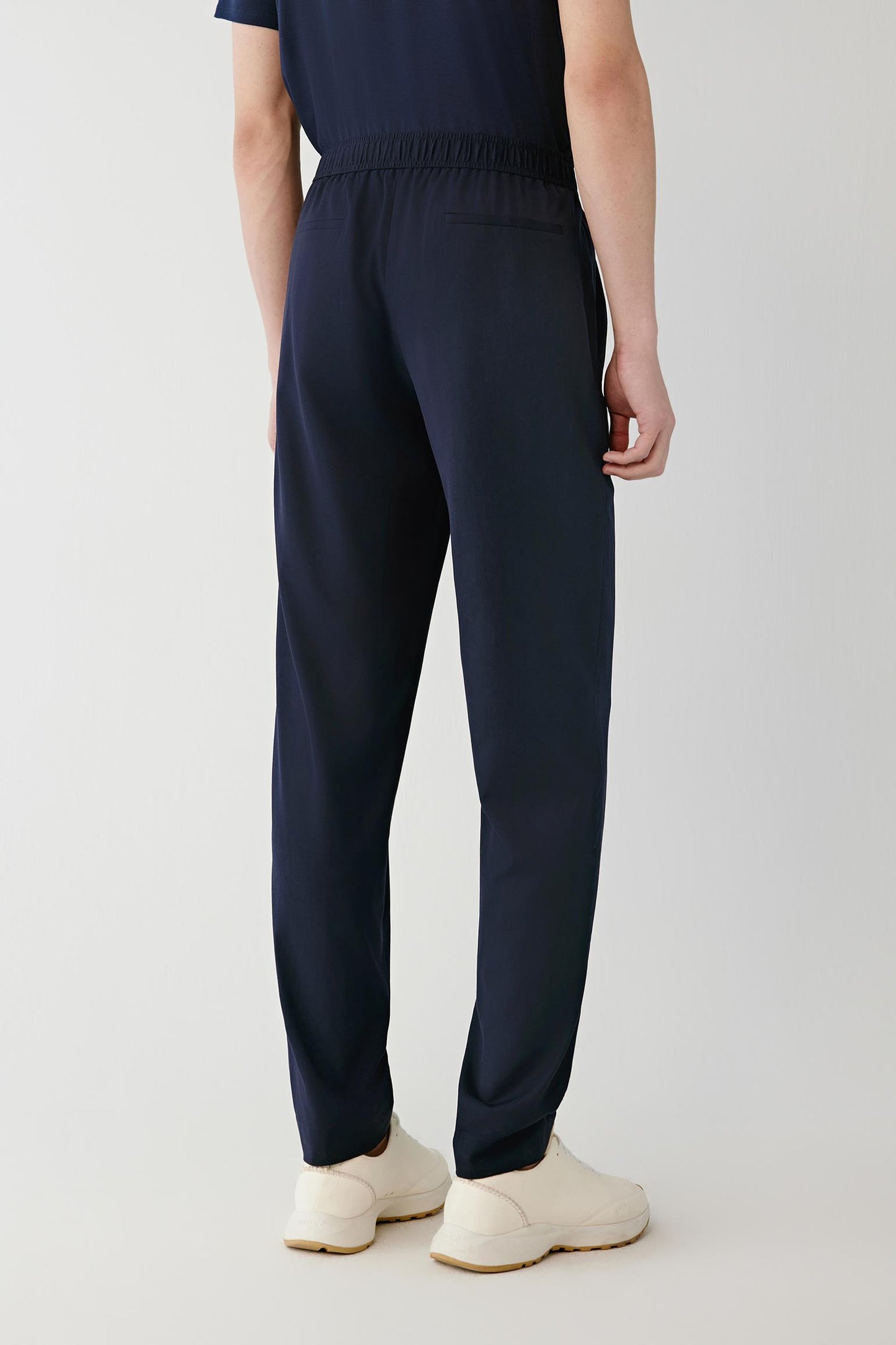 Back view of a man wearing navy tapered trousers with an elasticated waistband.