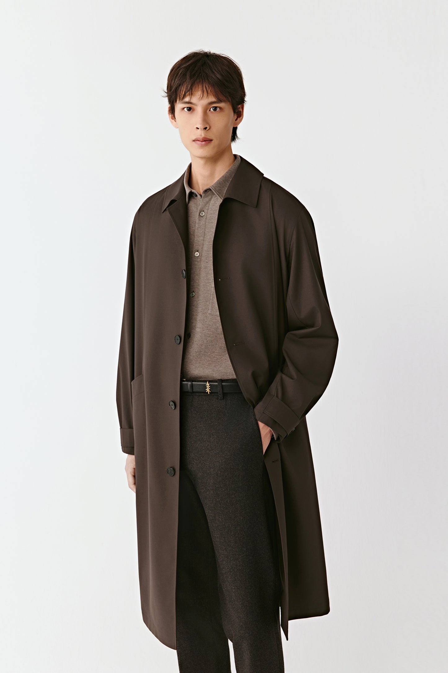 Man wearing a sienna brown worsted wool and silk trench coat with a straight, mid-length cut; three-quarter view highlighting the fluid drape, clean lines and structured collar.