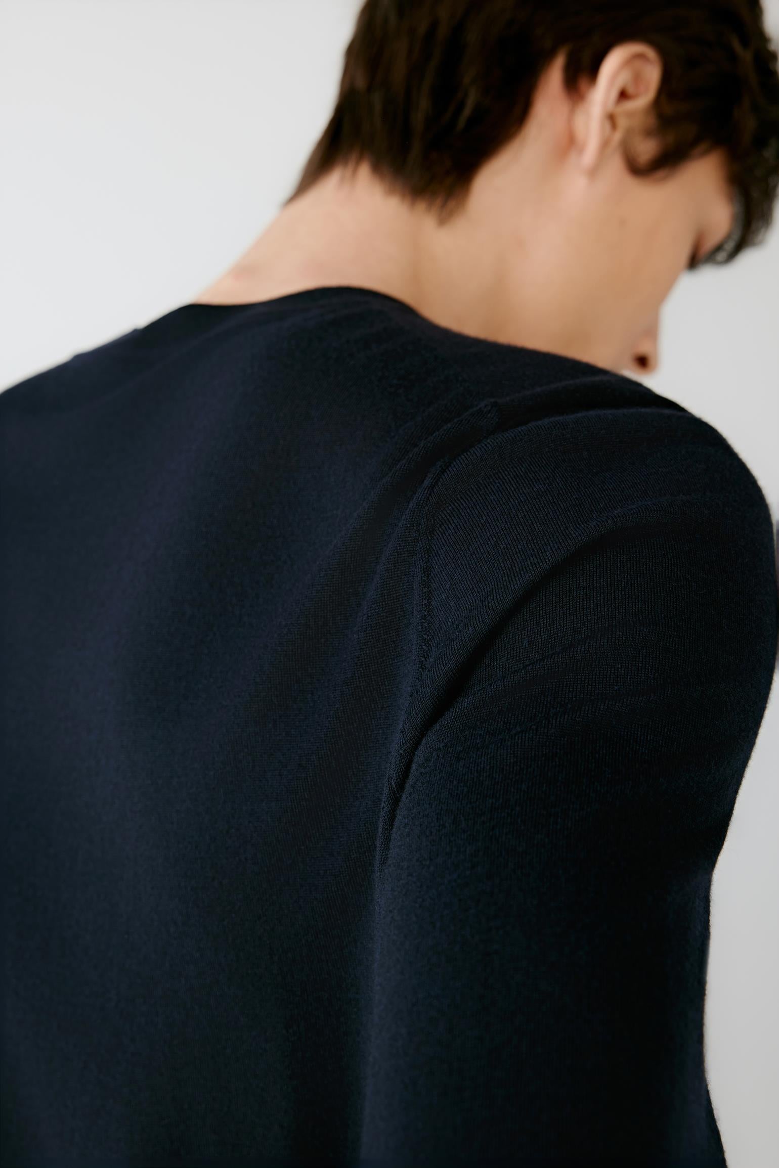 Close-up back view of a man wearing a dark navy long-sleeve knit top against a plain light background.