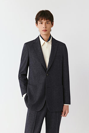 Full-length front view of a man in a blue melange jacket with a subtle denim texture, styled with matching trousers and a white shirt.