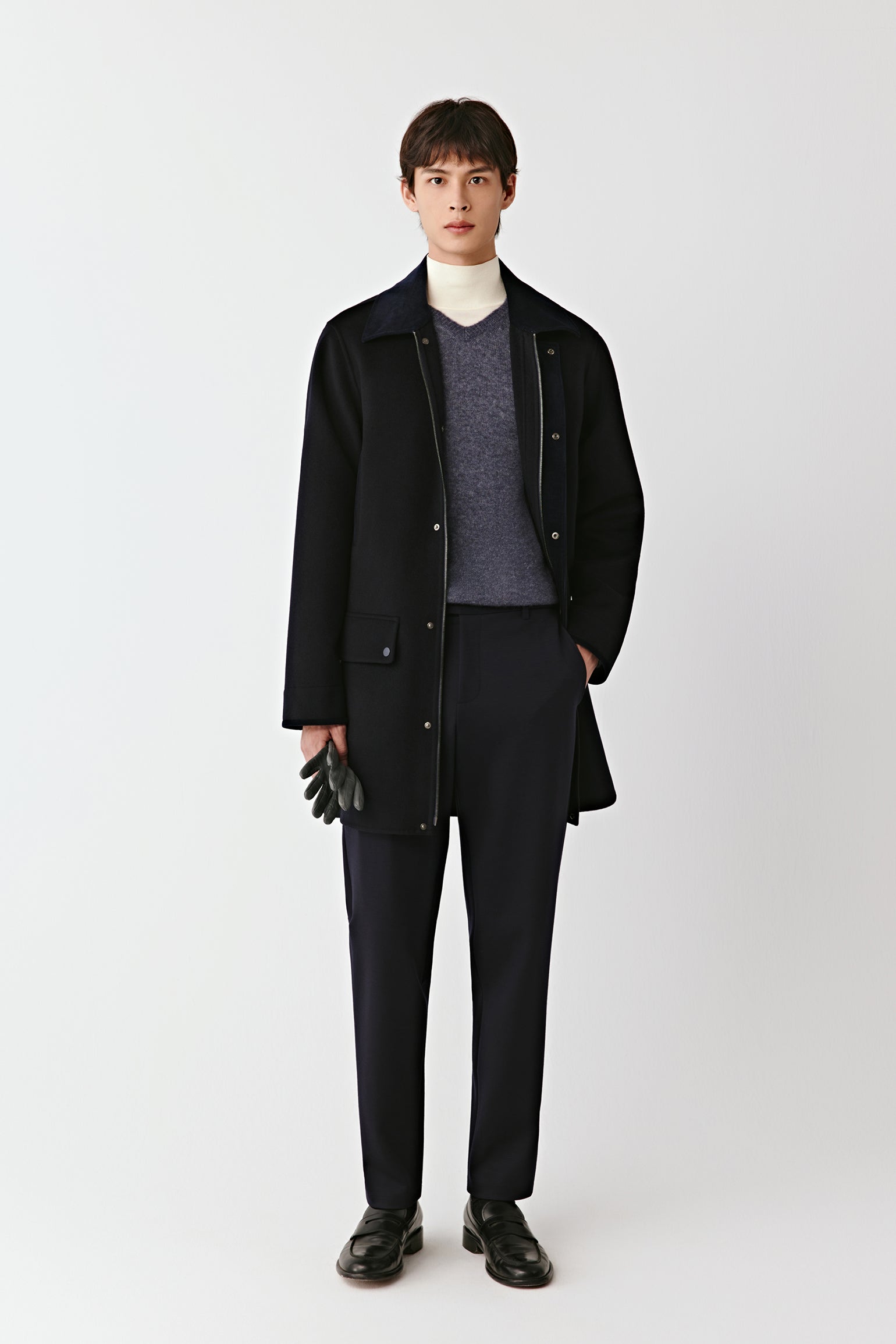 Man wearing a black coat, gray sweater, and black pants on a white background