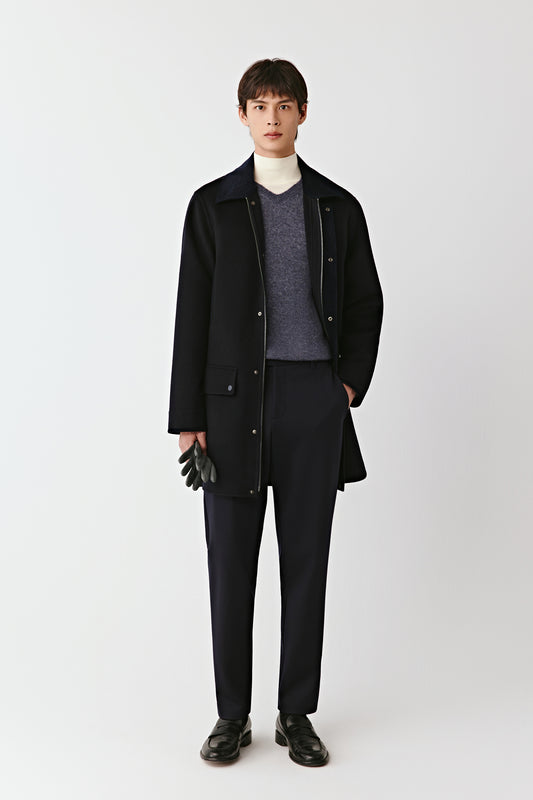 Man wearing a black coat, gray sweater, and black pants on a white background