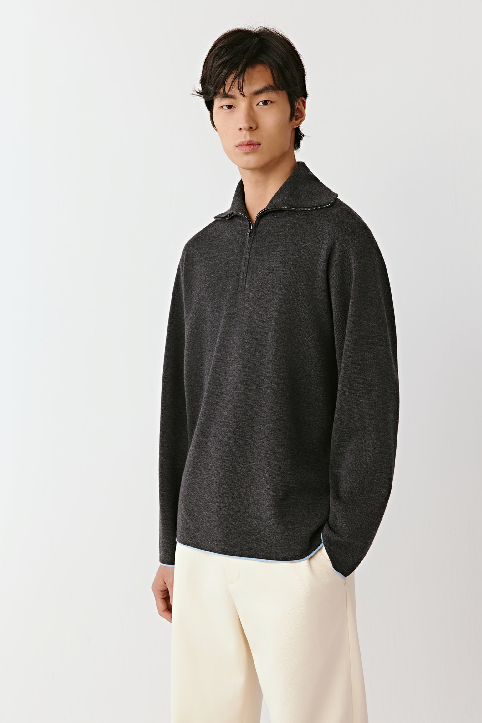 Man wearing a dark gray pullover with a high collar on a light gray background