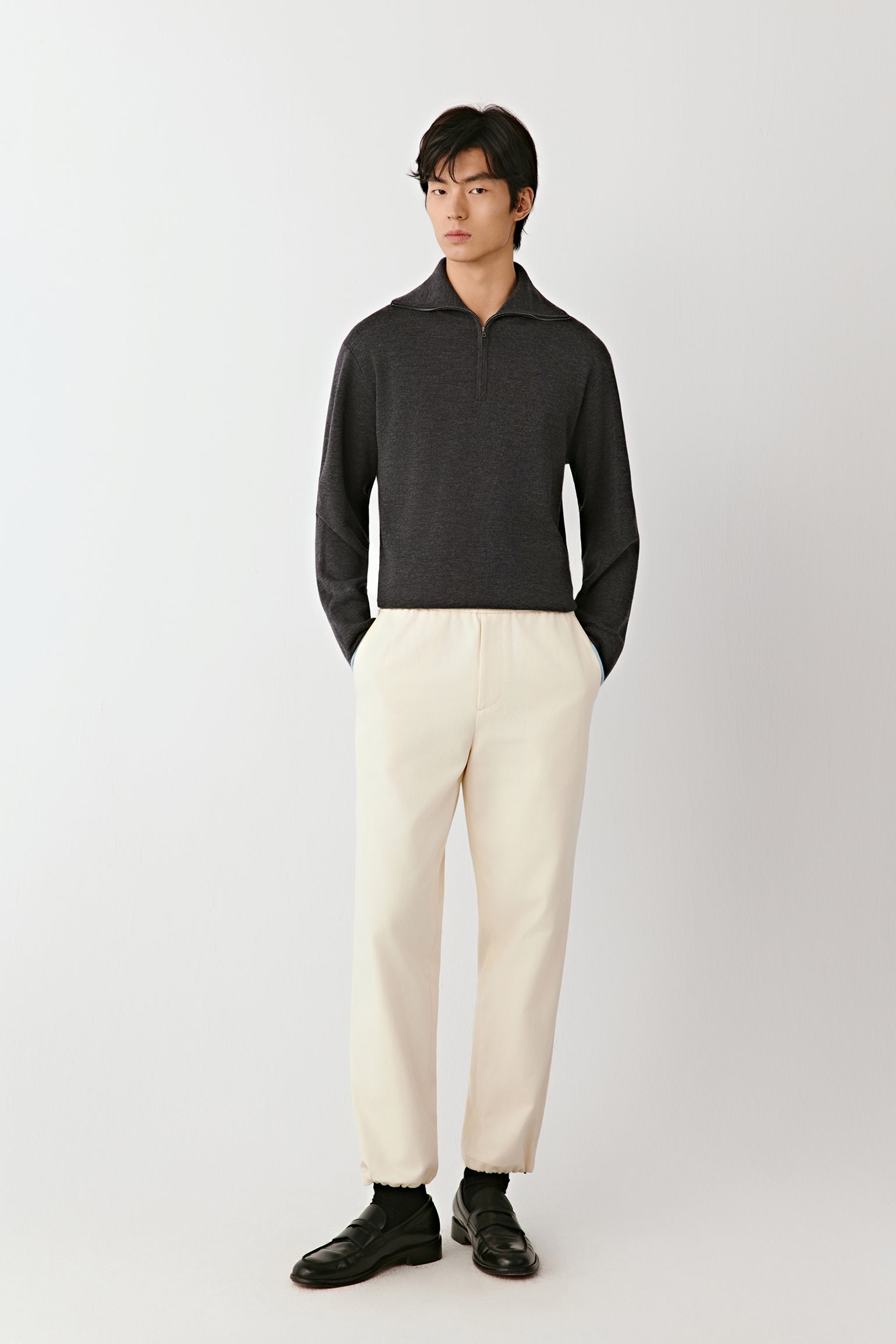 Man wearing a dark gray polo shirt and white pants on a white background