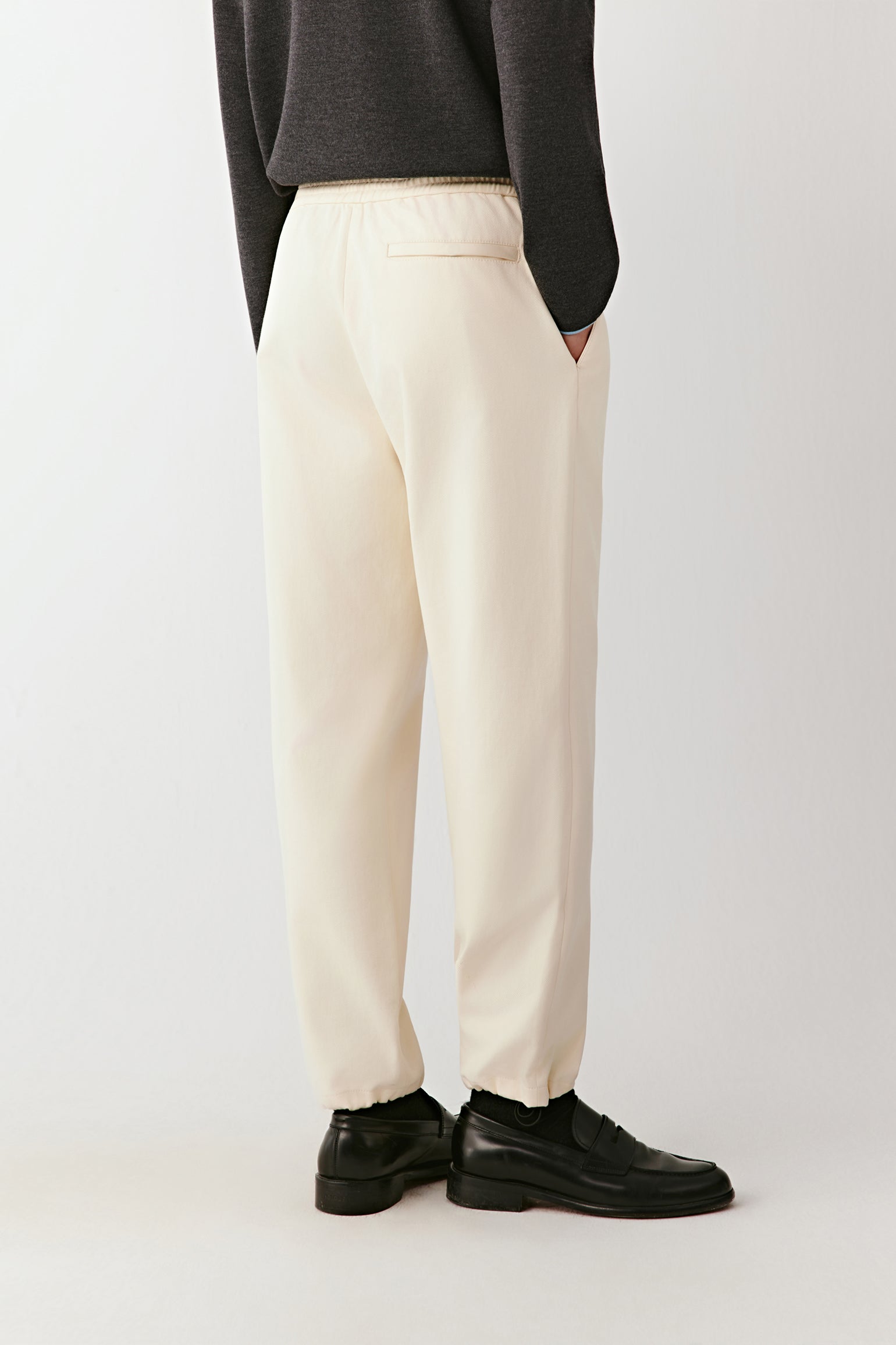 Person wearing white pants and black shoes on a plain background