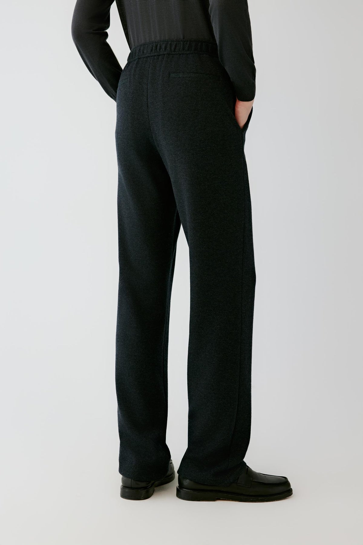 Three-quarter view of the black melange wool jersey trousers, showing the straight silhouette and structured jersey surface.