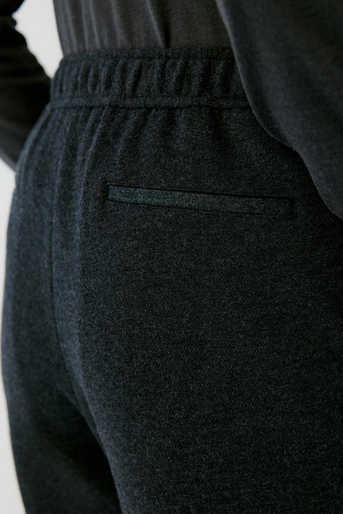 Close-up highlighting the back welt pocket, elasticated waistband and black melange jersey texture.