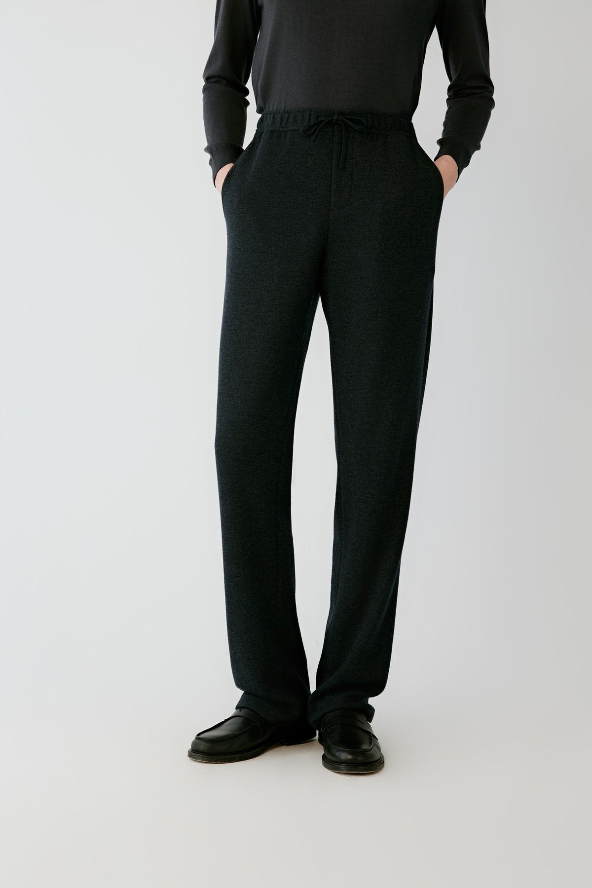 Front view of the black melange wool jersey trousers, highlighting the straight leg and side pockets.