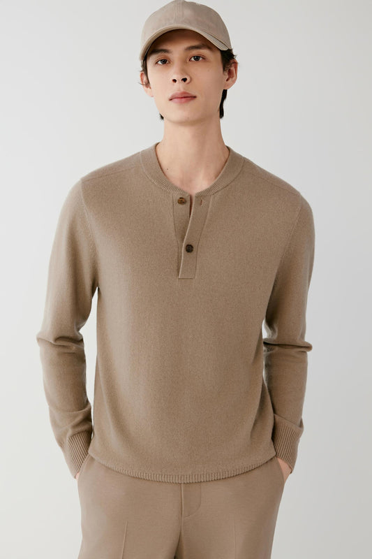 A man wearing a taupe brown knit henley sweater, matching trousers, and a matching cap, standing against a light gray studio background.