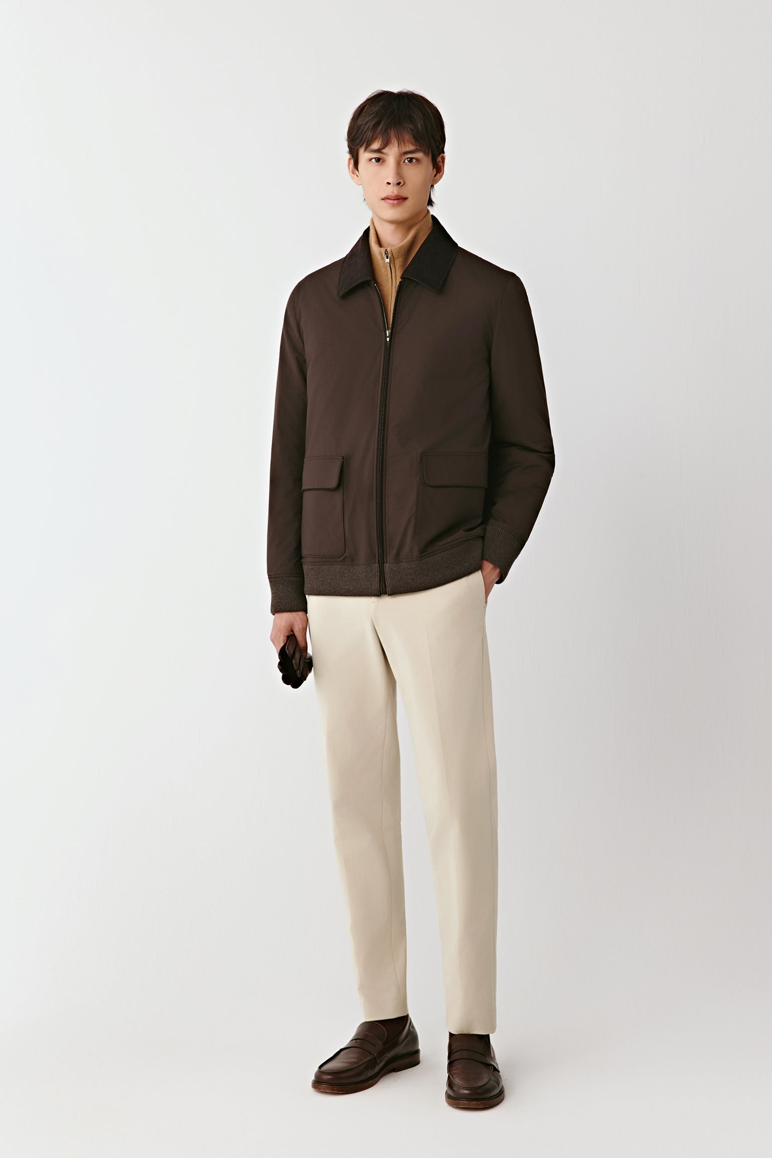 Front view of the deep brown worsted wool and yak jacket, featuring a shirt collar, zip fastening, and flap pockets, styled with off-white trousers.