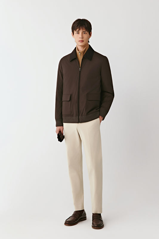 Front view of the deep brown worsted wool and yak jacket, featuring a shirt collar, zip fastening, and flap pockets, styled with off-white trousers.