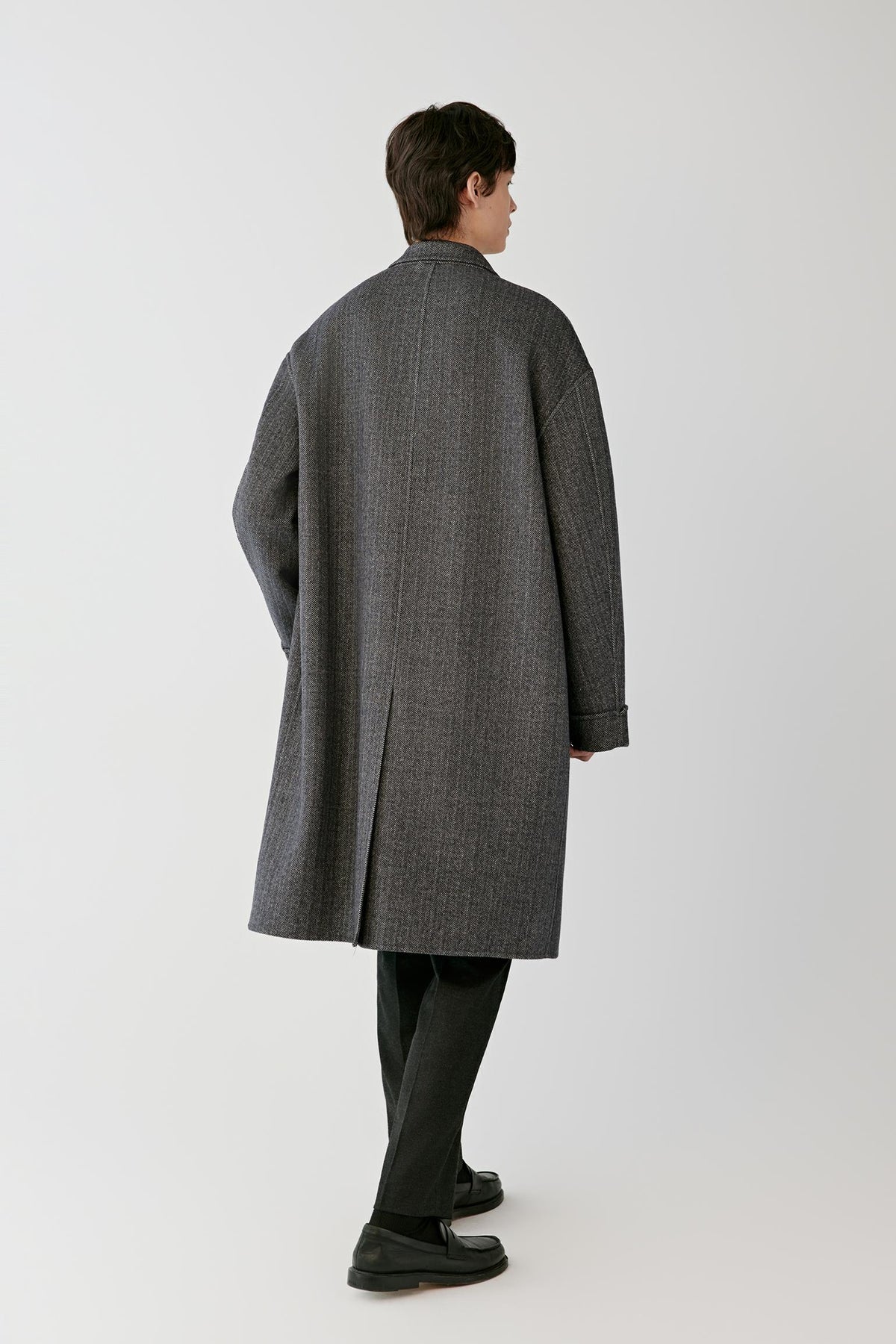 Back view of a man wearing the grey herringbone wool and cashmere coat, showing the long silhouette and centre back vent.