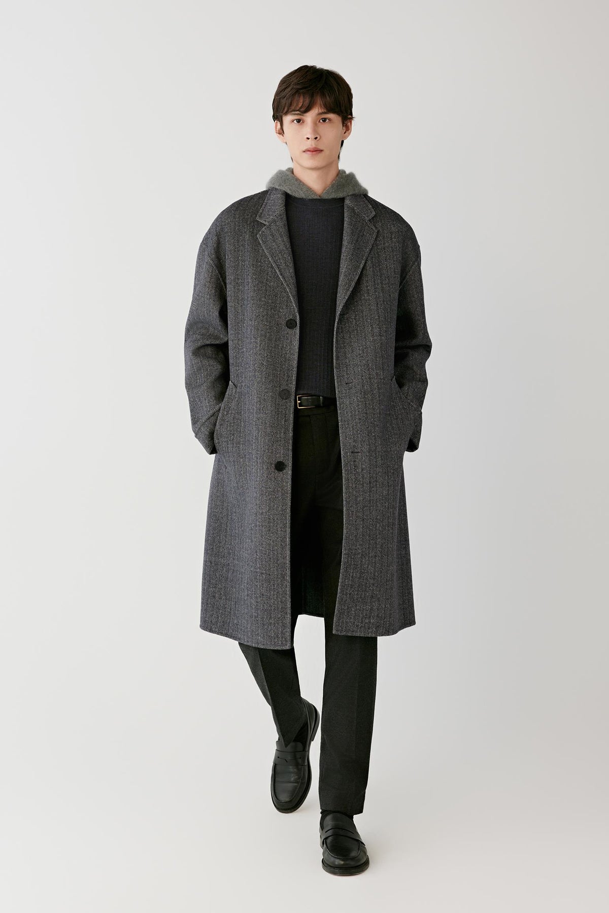 Front view of a man wearing a grey herringbone wool and cashmere coat, showing the relaxed silhouette, notched lapels and long length.