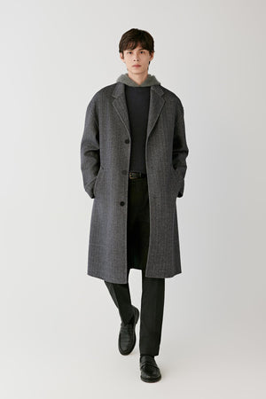 Front view of a man wearing a grey herringbone wool and cashmere coat, showing the relaxed silhouette, notched lapels and long length.