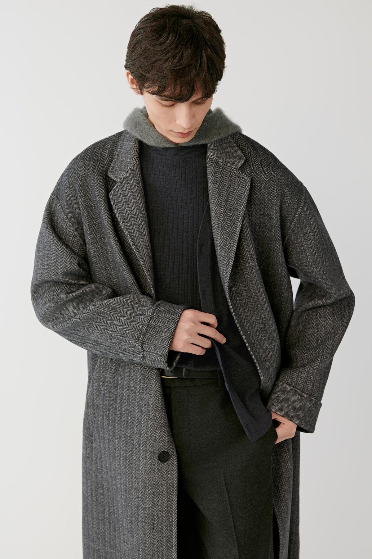 Three-quarter view of a man wearing the grey herringbone wool and cashmere coat, highlighting the relaxed silhouette and textured herringbone weave.