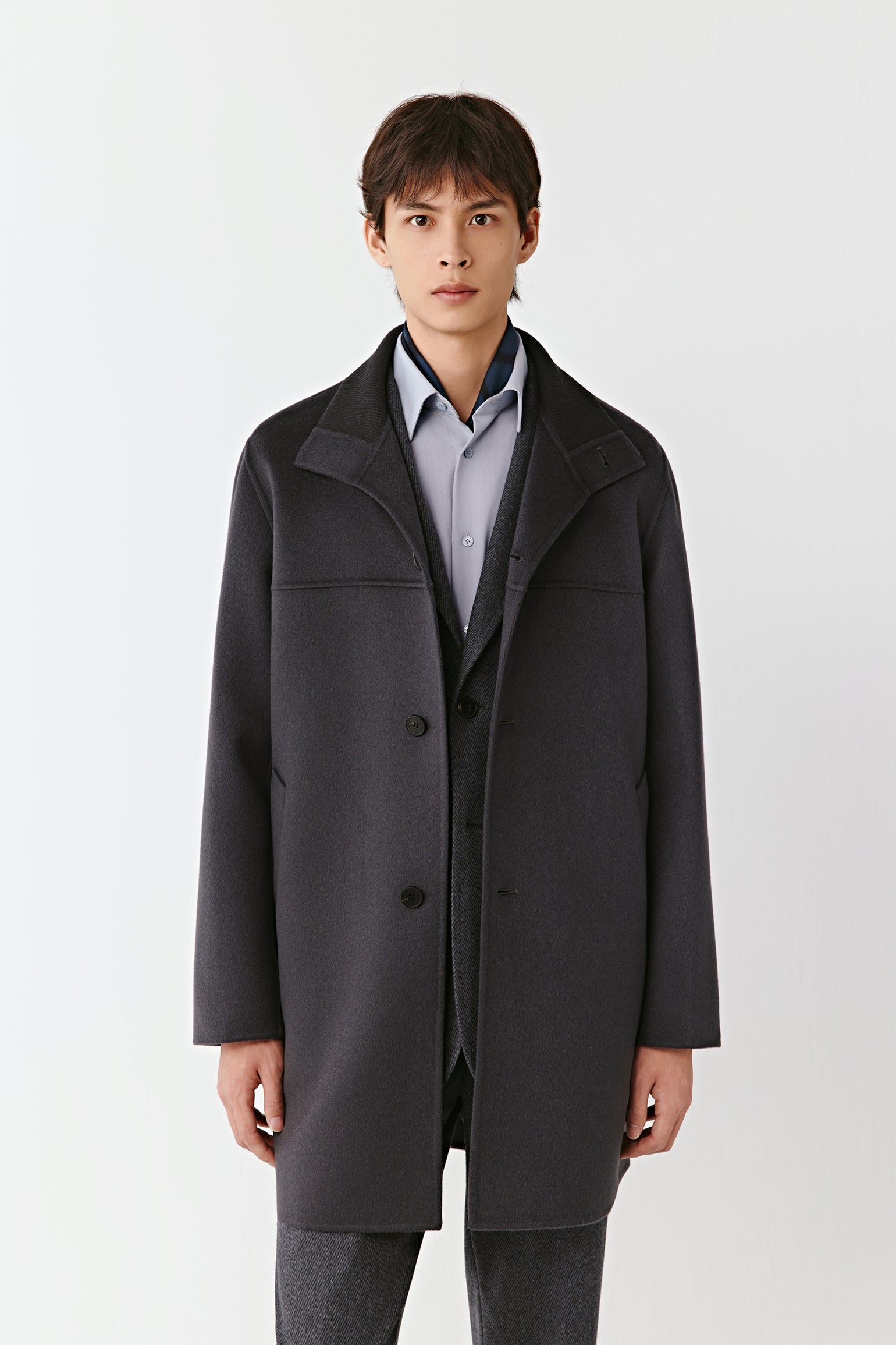 Man wearing a dark gray coat over a light shirt on a white background